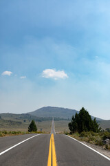 A very long tarmac road going in to the mountains in the distance which are covered in haze, but...