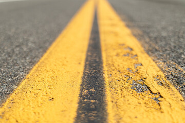 A close up of a double yellow line of a slightly beat up with cracks tarmac road in the desert