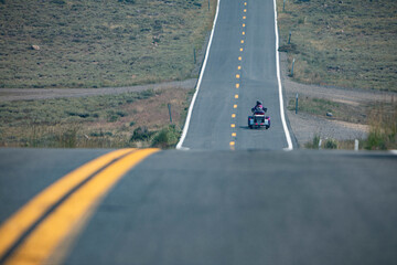 A person traveling on a three-wheeled motorcycle on a long tarmac road on a hot Summer day. Nr.1