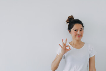 Asian Thai woman showing ok good hand gesture, happy smiling looking at empty space, advertising standing isolated over white background wall.