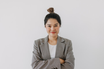 Asian Thai woman smiling and crossing her arms on chest, looking at camera, businesswoman wearing blazer suit and bun hairstyle, successful at work, standing isolated over white background wall.