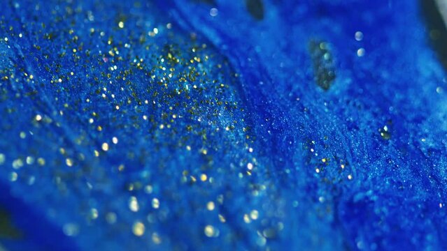 Wet glitter spill. Gel drip. Defocused blue golden color shimmering particles texture emulsion flow motion abstract art background.