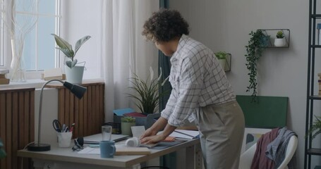 Young African American woman student cleaning desk sorting books tidying living room in apartment. Housework and domestic chores concept.