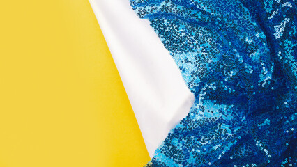 White satin or silk fabric with blue sequins on yellow background. Glitter texture is the trend of...