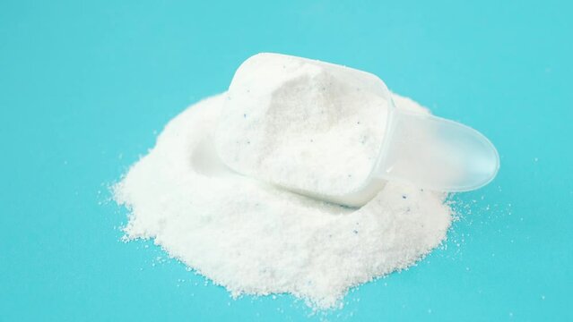 Female hand holds a scoop with white washing powder on a blue background close-up.