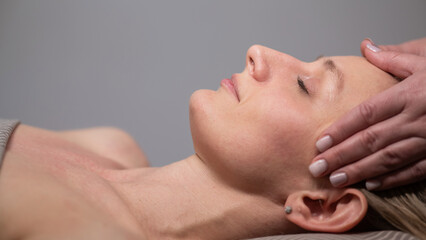 Caucasian woman undergoing head and face massage procedure. 