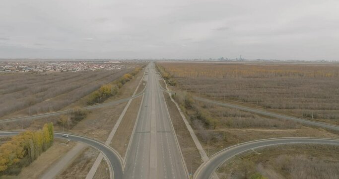 Car alone driving on by crossroads four-way clover-shaped highway intersection with a bridge amid an agricultural landscape and arid steppe. View from a drone on a cloudy autumn day