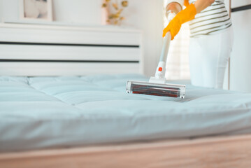 Housekeeper cleaning mattress with electronic vacuum cleaner in bedroom