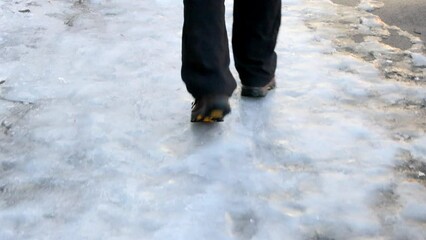 the legs of a man walking on an icy sidewalk on a winter evening, rear view 4k video