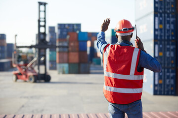 back view African factory worker or engineer using walkie talkie and showing stop gesture to crane car in containers warehouse storage - obrazy, fototapety, plakaty
