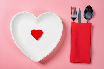 A heart plate with a red heart and silverware of fork, knife, and spoon in a red napkin