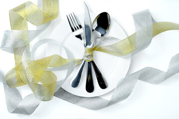 White plate with silverware of fork, knife, and spoon tied up on ribbon