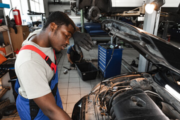 Young African male mechanic repairs car in garage close up