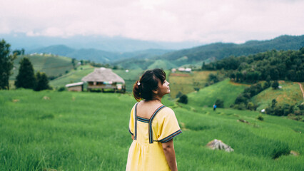 The hill tribe woman walks in the rice paddies feel relaxing and enjoying in the meadow. Female in Traditional Dress in the rice field terrace ,bamboo house background. Ban Pa Bong Piang, Chiangmai.