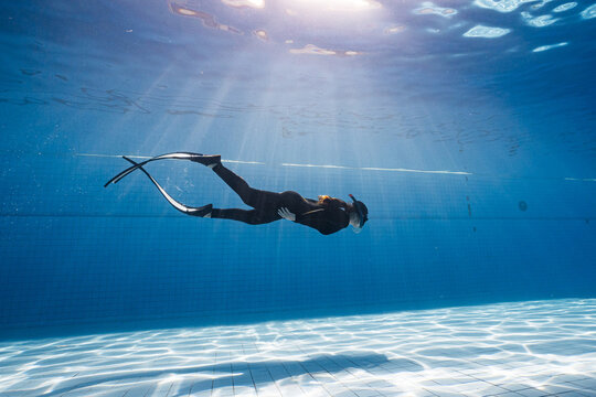 Beauty freediver Asian women diver with fins glides underwater in transparent blue pool. Freediver glides over swimming pool with black fins. Attractive woman free diver in blue pool.