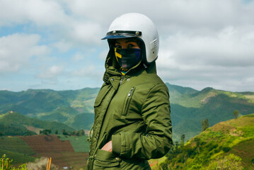 Female motorcyclist standing with her enduro motorcycle on mountain top, peaks skyline view and...