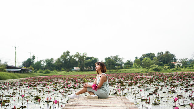 Asian women sitting in lotus field pond. Portrait of smiling woman with big grin. woman in flower lotus lake, Scenic beautiful view nature Landscape, Red lotus sea Nakhon Nayok, Thailand.