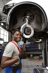 African male auto-mechanic repairing car brakes under the car in auto service