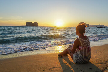 Asian Young woman in cute summer dress sitting, looking at sunset rise the sea. Smile Freedom and...