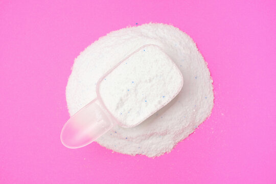 White washing powder in a measuring spoon on pink background top view close-up.