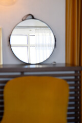 A window with a curtain is reflected in a round mirror on the wall