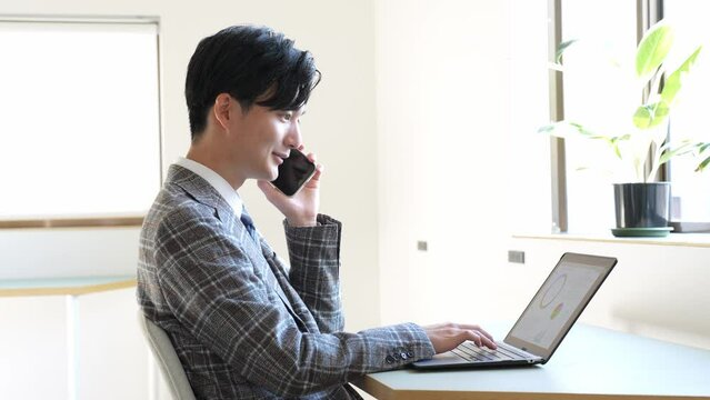 携帯で話しながらパソコンを見る若い男性