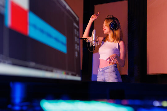 Young professional female singer with headphones performs a song with a microphone while recording in a music studio