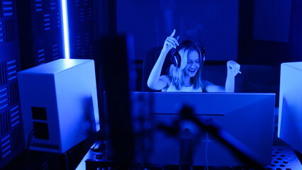 A young smiling woman wearing headphones speaks into a microphone at a radio station.