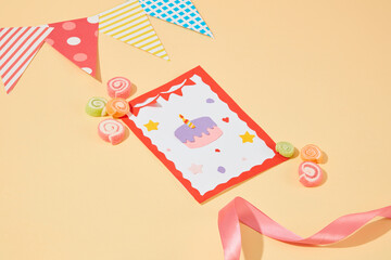 A cute birthday card decorated with gummy candy, a triangular flag and ribbon on a pastel background. Design birthday wishes with the meaning of luck.