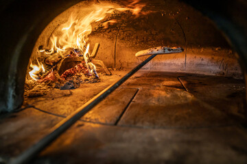 Traditional oven for baking pizza with burning wood and shovel. Neapolitan pizza is finished on a...