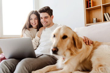 Portrait smiling couple hugging, dog, golden retriever, selective focus using laptop online shopping