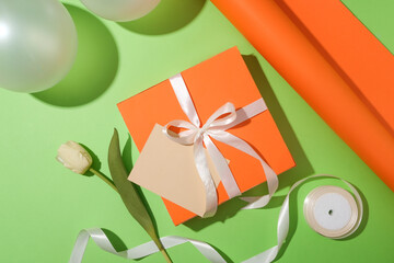 On a pastel green background, a gift box decorated with a bow-tied ribbon, a card and a tulip....