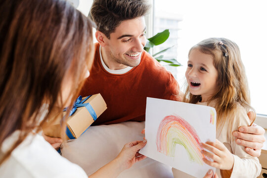 Portrait of smiling young family. Handsome father, mother and little daughter holding drawing