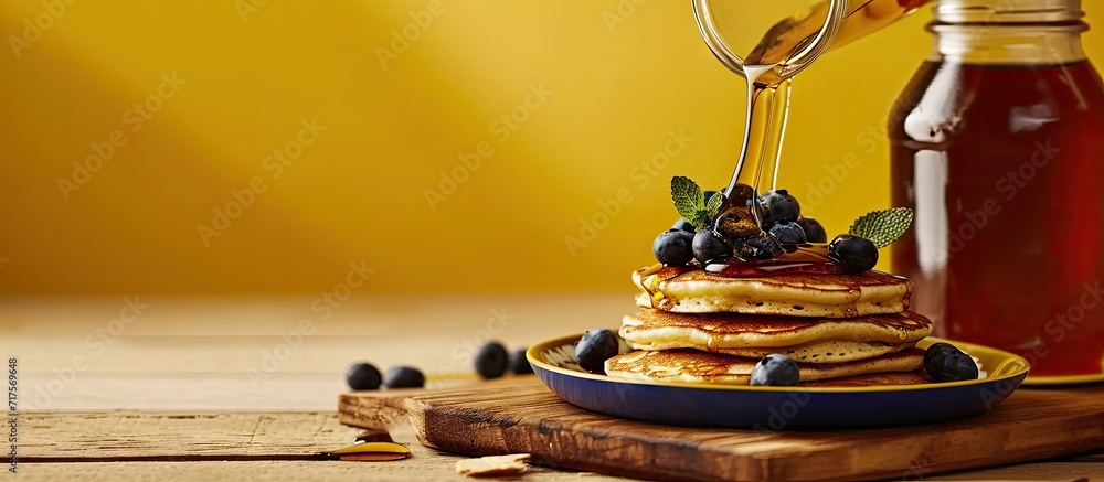 Aufkleber horizontal image of maple syrup pouring onto pancakes and blueberries on yellow with copy space food
