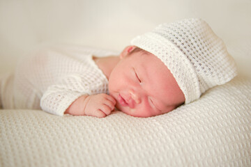 ​Happy smiling newborn baby in white blanket, sleeping happily in white suit and hat. Photo shoot...