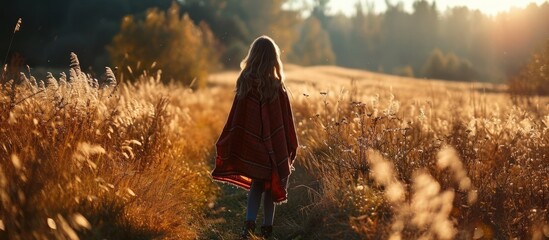 Girl in poncho travel alone in field with a view in sunlight Warm autumn weather calm scene Wanderlust photo series. Copy space image. Place for adding text or design - obrazy, fototapety, plakaty