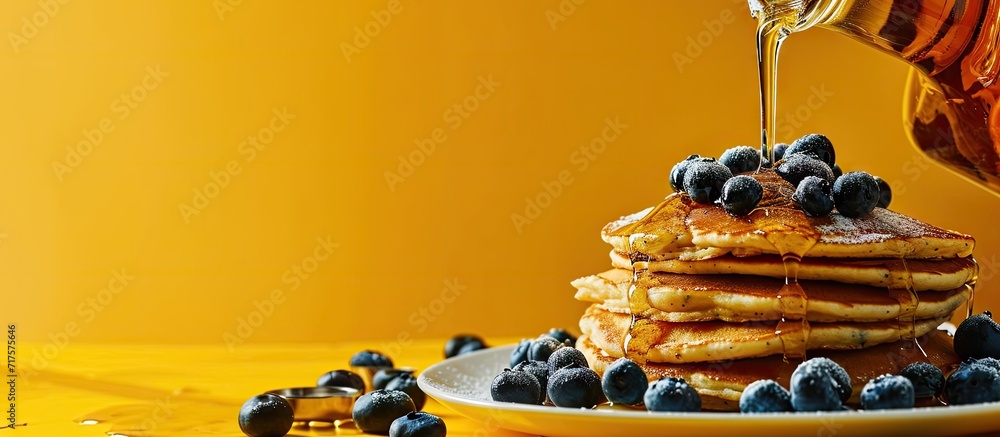 Poster Horizontal image of maple syrup pouring onto pancakes and blueberries on yellow with copy space Food organic ingredients and healthy eating. Copy space image. Place for adding text or design
