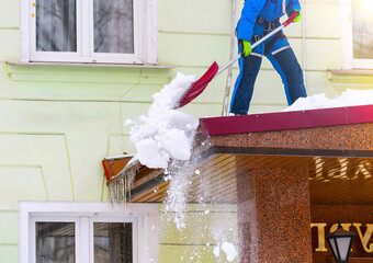 Removing snow from the roof of a building with a shovel in winter. Services for cleaning roofs from...