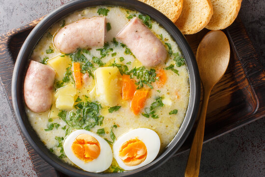 Polish zurek a rich soup soured with fermented rye starter, served with a boiled halved egg and a meaty white sausage close-up in a bowl on the table. Horizontal top view from above