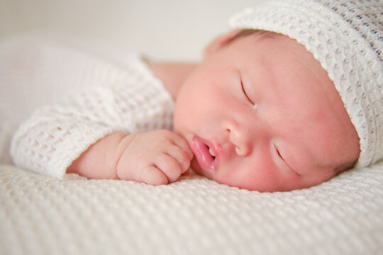 Close up of sweet face of a newborn boy. The asian baby boy wearing white suit and lying in a white blanket