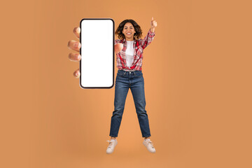 Excited young arab woman jumping in the air with smartphone
