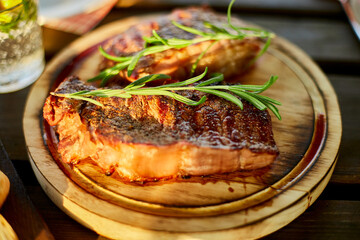 A succulent ribeye steak, perfectly grilled and adorned with fresh rosemary sprigs, rests on a circular wooden plate against a dark, rustic backdrop.