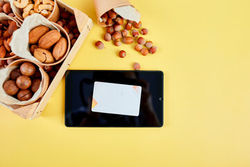 An assortment of nuts displayed next to a tablet on a vibrant yellow background highlights an online nut sale.