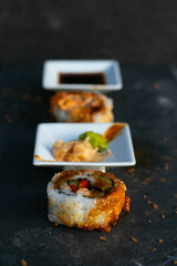 Sushi and condiments in a row on a dark bench.