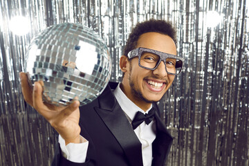 Portrait of overjoyed black man in suit and glitter glasses hold disco ball celebrate in nightclub....