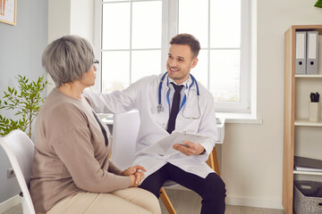 Fototapeta premium Young smiling doctor clinic visit, male nurse taking care of old woman during regular check, examination. Man monitoring resident of nursing home, patient in hospital, maintain elderly health, safety