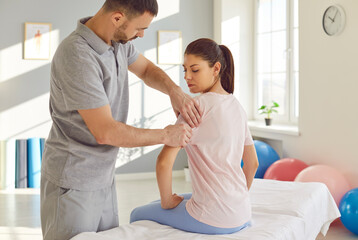 Young male professional chiropractor or physical therapist massaging young Caucasian woman's arm...