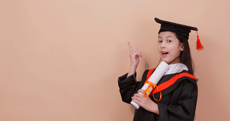 A school girl wearing a graduation gown makes happy gestures and expressions. Isolated on brown background in studio.