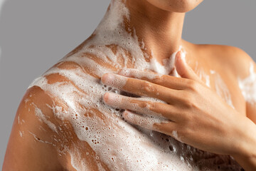 Cropped closeup on woman washing her body with soap foam