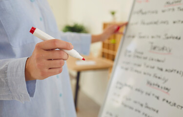 Female hand holding red marker handwriting close up, writing at wipeable board with white surface for teaching or presentation, meeting exchange information, office ideas brainstorming 